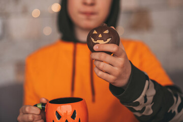 Portrait of candid authentic zoomer boy posing with jack lantern mug and sweets at halloween party