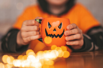 Portrait of candid authentic zoomer boy posing with jack lantern mug and sweets at halloween party