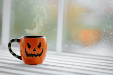 Close up of cup in shape of pumpkin Jack lantern with hot coffee on windowsill