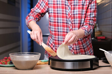 Woman cooking delicious crepe on electric pancake maker in kitchen, closeup
