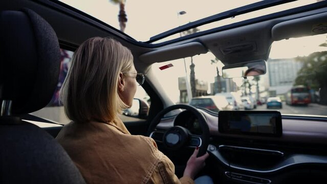 Blonde woman driving car, sunroof open to reveal palm trees, embodying a sense of adventure and exploration in the city