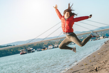 Young smiling woman jumping for joy at riverside on a sunny day. Beautiful woman feeling an ultimate freedom while enjoying outdoors.