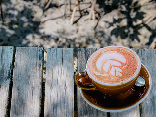 Close-up coffee cup with leaf shaped latte art on wooden background. Building exterior.
