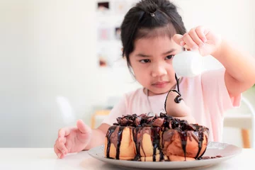 Fotobehang 4-5 year old ,Cute asian girl is smile and pouring chocolate on chocolate toast on white table in a coffee shop,Honey Toast is a sweet dessert that children love, Relax happy family time concept © ISENGARD