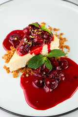 side view of cheesecake with juicy berries and mint on a white plate