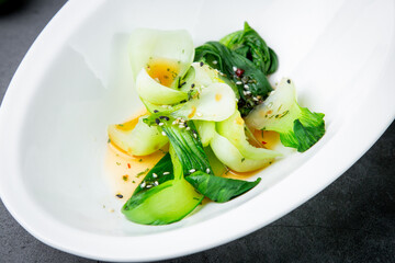 bok choy cabbage with sesame seeds and sauce in a white plate, top view