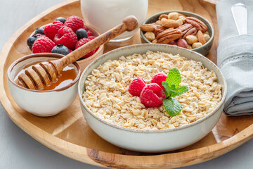 Bowl of porridge or oatmeal with different ingredients on wooden tray. Breakfast serving. - obrazy, fototapety, plakaty