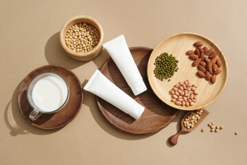 Unbranded tubes decorated with a dish of green beans, peanuts and almonds. A cup of milk placed on a wooden dish. Healthy and skincare concept