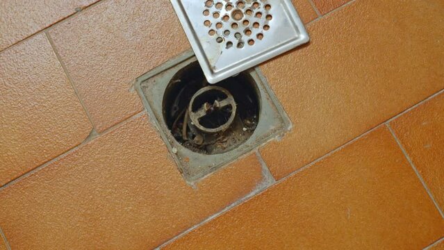 Dirty old water floor drain with opened strainer, brown tiles flooring