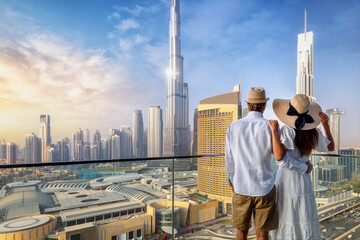 A couple on holidays enjoys the panoramic view over the city skyline of Dubai, UAE, during sunrise - obrazy, fototapety, plakaty