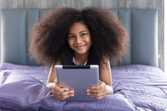 African black child girl afro hair cute lovely lay on bed with tablet computer happy self learning at home holiday, portrait smiling looking camera.