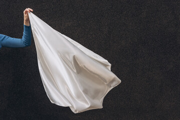 White silk scarf in woman's hand floating on the wind on dark grey background. Lifestyle.