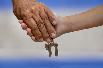 Am Israel Chai. Hands of an elderly man holding the hand of a child close up. they holding a silver Chai key chain, which spell "life" in hebrew. Blue and White background, Israel flag