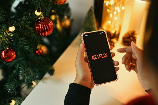 Chiang Mai, Thailand - Oct 31,2023: Woman holds a smartphone with the Netflix logo displayed on the screen near Christmas tree