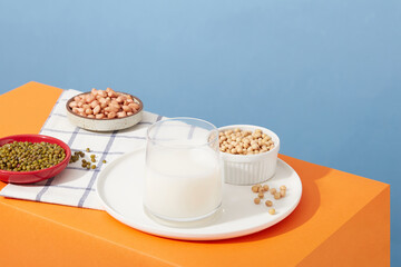 Soybeans, peanuts and green beans are contained inside dishes and a bowl. Glass cup filled with nut milk. Different types of nuts may have slightly different micronutrient