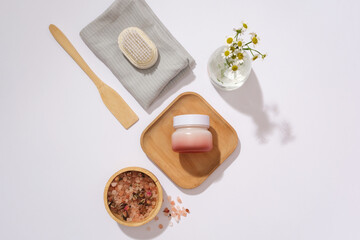 An unlabeled cosmetic jar is placed on a wooden tray, surrounded by props. Mockup for natural cosmetics advertisement with main ingredient from pink salt.