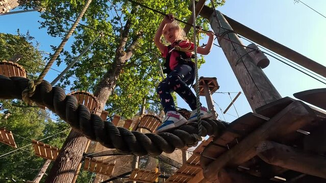 Happy Little Girl Playing in Tarzan Attraction on Playground in Amusement Park. Little Girls Enjoy Playing and Climbing in Summer Adventure Park. Sunny Day 4K Video