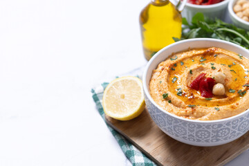 Roasted red pepper hummus in white bowl on white marble background. Copy space