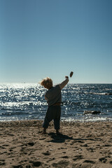 A little three-year-old blond boy is throwing a stone into the sea.