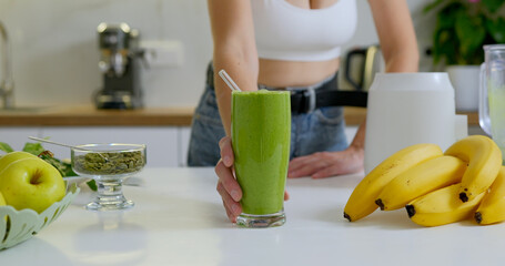 Sporty woman with glass of green vegan smoothie.