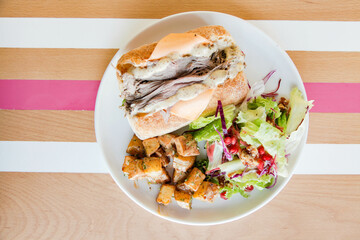 Roast beef open faced sandwich on a plate served with veggies on the side on a wooden table with stripes.
