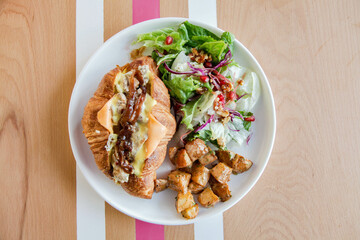 Chicken croissant open faced sandwich with veggies on the side.