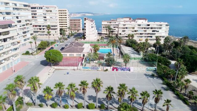 Drone aerial over park with palm trees, sport field and moving to apartment buildings at Cabo Cervera,Torrevieja and La Mata beach
