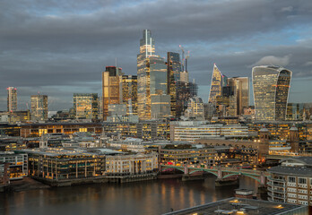 Obraz premium Aerial view of The skyscrapers in the business district of London with the River Thames on foreground at sunset. Architectural modern buildings of the City of London, Space for text, Selective Focus.