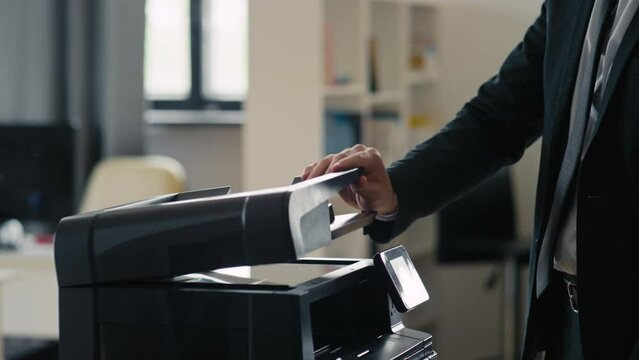 Side shot of unrecognizable office worker taking document and its copy from printer and leaving in office