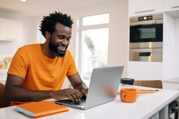 Smiling African American Freelancer in an Orange T-Shirt Working at Home on a Laptop