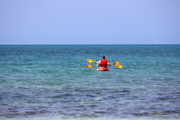 Fototapeta na wymiar Kayaking in the sea, couple wearing life vests rowing with paddles in canoe. Man and woman in one team, travel and water sports