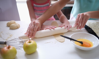 Obraz na płótnie Canvas Mom and daughter roll out the dough with rolling pin in kitchen. Family cooking pastry concept
