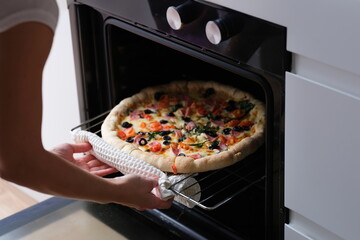 Woman puts pizza pan in oven. Cooking pizza at home concept