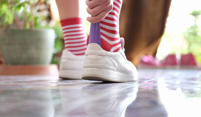 Man in striped socks putting on white sneakers with shoehorn closeup. Shoe accessories concept
