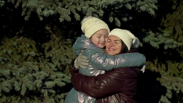 Young woman and her daughter, 7-8 years old, look at each other with love and tenderness. On a walk in the winter forest.