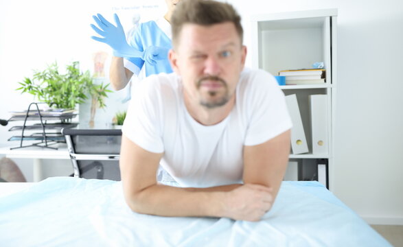 Doctor putting on protective glove for rectal examination of man. Hemorrhoid treatment concept