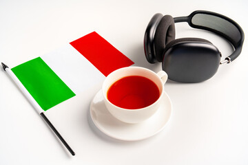 Flag of Italy, cup of tea and headphones on white background