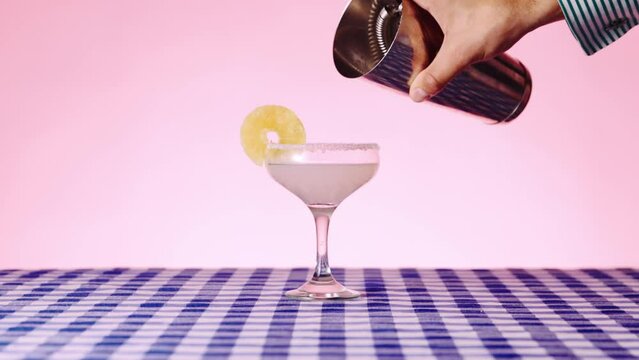 Sweet and sour margarita cocktail on checkered tablecloth over pink background. Bartender pouring lime juice into tequila. Concept of cocktails, alcohol drink, bar, taste, menu, pop art style.