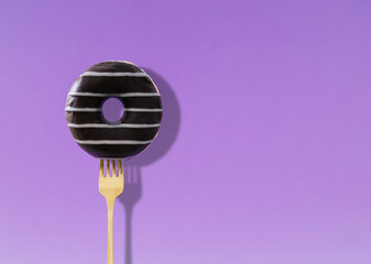 Yummy donut pricked on a fork on light violet background. Creative art. Contemporary style. Minimal concept of food with copy space for text. Donut aesthetic.