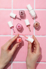 Nail polishes in female hands on pink background, top view