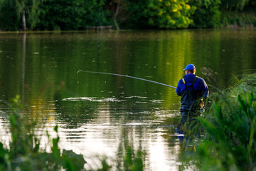 Fototapeta na wymiar Middle aged fisher-man standing with fishing rod in the pond