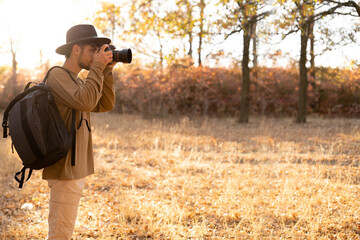 Professional young photographer man taking pictures with digital camera equipment of nature on sunset.