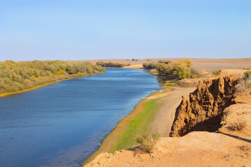 Colorful autumn landscape. View of the river from above from a cliff, with a dirt road and a clear blue sky. Panorama. Nature of the autumn season, scenic beauty.