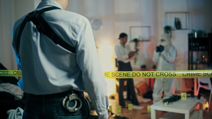 The back view of a detective entering the crime scene where his colleagues examine the evidence
