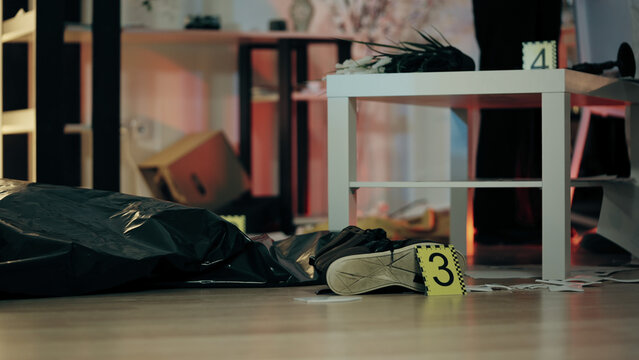 A dead body in a plastic bag is lying on the floor of a trashed flat at the crime scene, with marked evidence