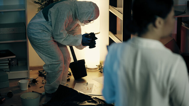A detective and a forensic expert are working at the crime scene while examining the trashed room