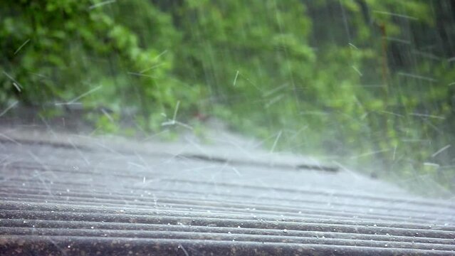 summer rain with hail falls on the slate roof against the background of trees with green foliage