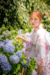 Portrait of a young woman wearing a Japanese yukata summer kimono in a hydrangea garden. Kyoto,...