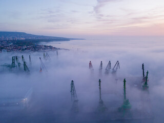 Aerial view of port cranes protruding through the morning fog