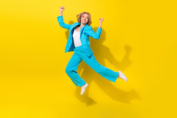 Fototapeta na wymiar Full length photo of positive satisfied woman wear blue stylish suit clenching fists flying win lottery isolated on yellow background